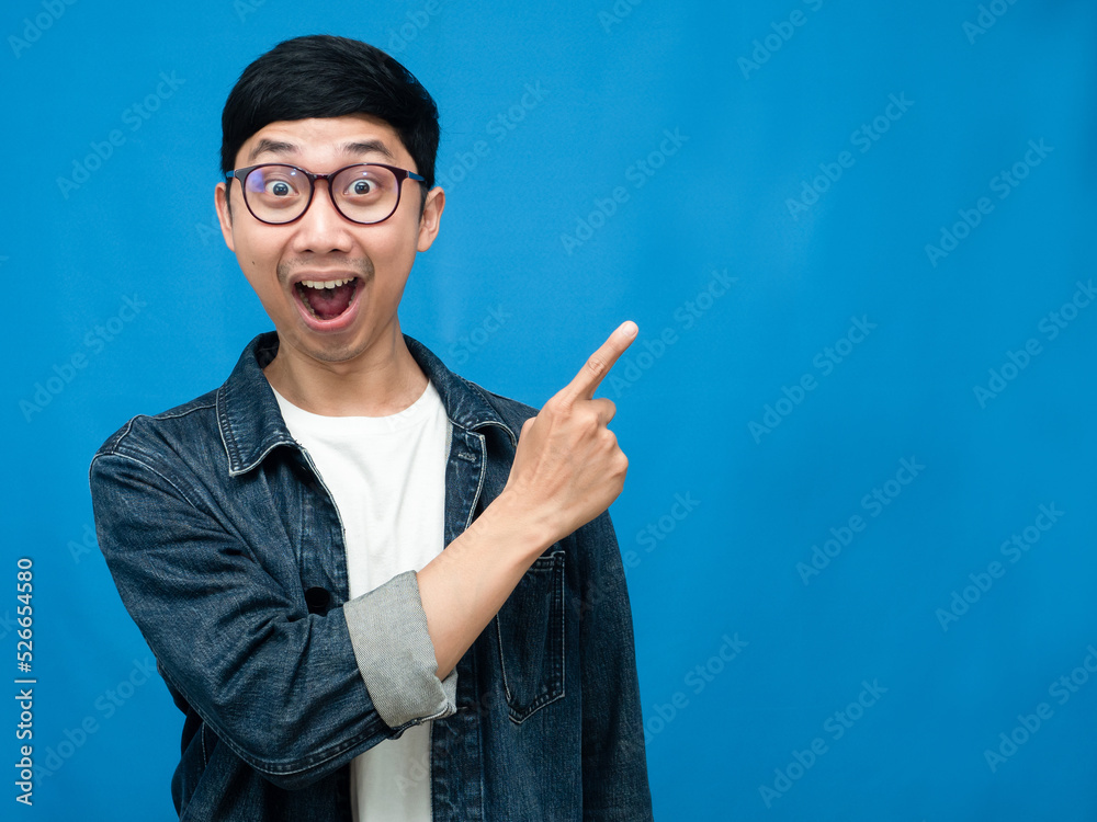 Positive man jeans shirt gesture point finger at copy space blue background Positive man jeans shirt gesture point finger at copy space blue background