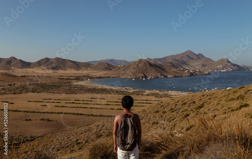Rear view of a boy with backpack looking at view of the bay. Cabo de Gata Nature Park, Almeria, Spain © WeeKwong