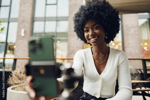 Portrait of smiling woman with afro hairstyle on video call sitting in cafe