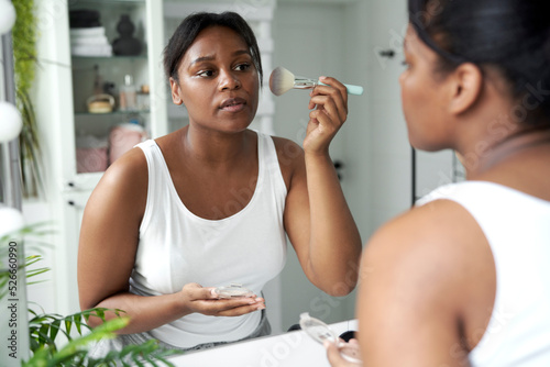 African-American woman applying make up blusher in the bathroom photo