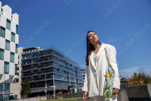 Attractive woman in trendy outfit standing on skyscrapers cityscape background and looking away