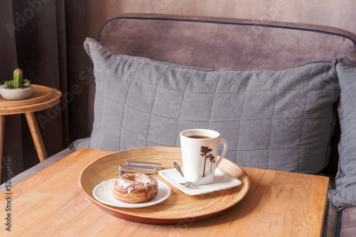 Fototapeta Naklejka Na Ścianę i Meble -  On a wooden small table on a tray, a cup and a saucer of morning fragrant coffee and a delicious brewed ring.