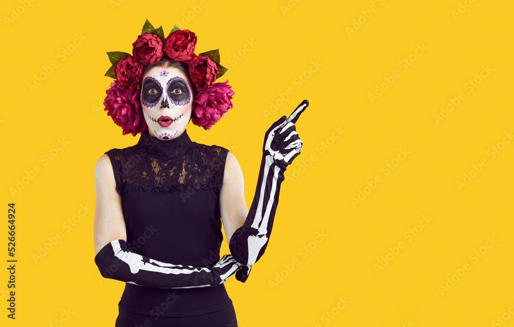 Woman in Halloween costume with surprised expression showing copy space advert solution. Woman in peony wreath, Halloween makeup and gloves in form of hand brush advertises on orange background. Woman in Halloween costume with surprised expression showing copy space advert solution. Woman in peony wreath, Halloween makeup and gloves in form of hand brush advertises on orange background.