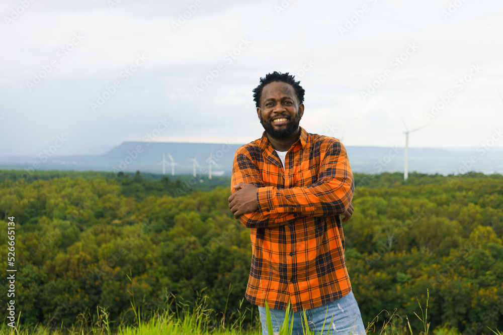 Portrait of black man smiling to camera at rural outdoor with wind turbine as background.
