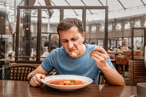 dissatisfied unhappy customer of the restaurant sniffs the disgusting smell of a bowl of soup with spoiled ingredients and is going to complain to the chef photo