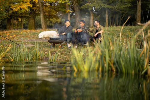 Multiracial male friends having a picnic and fishing on river or lake coast. Concept of leisure and weekend in nature. Idea of friendship and enjoying time together. Autumn day