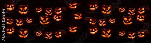 Scary Halloween celebration holiday card - Many spooky carved pumpkins on dark wooden wall background banner panorama.