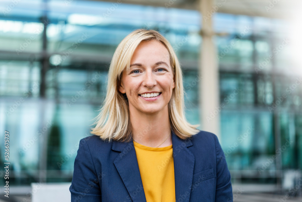 Smiling blond businesswoman in front of building Smiling blond businesswoman in front of building