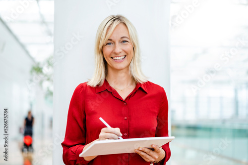 Smiling businesswoman with tablet PC and digitized pen standing in front of column