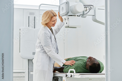 Smiling radiologist talking with patient lying on X-ray machine in clinic