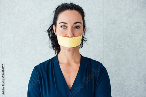 Woman with tape over mouth standing in front of gray wall
