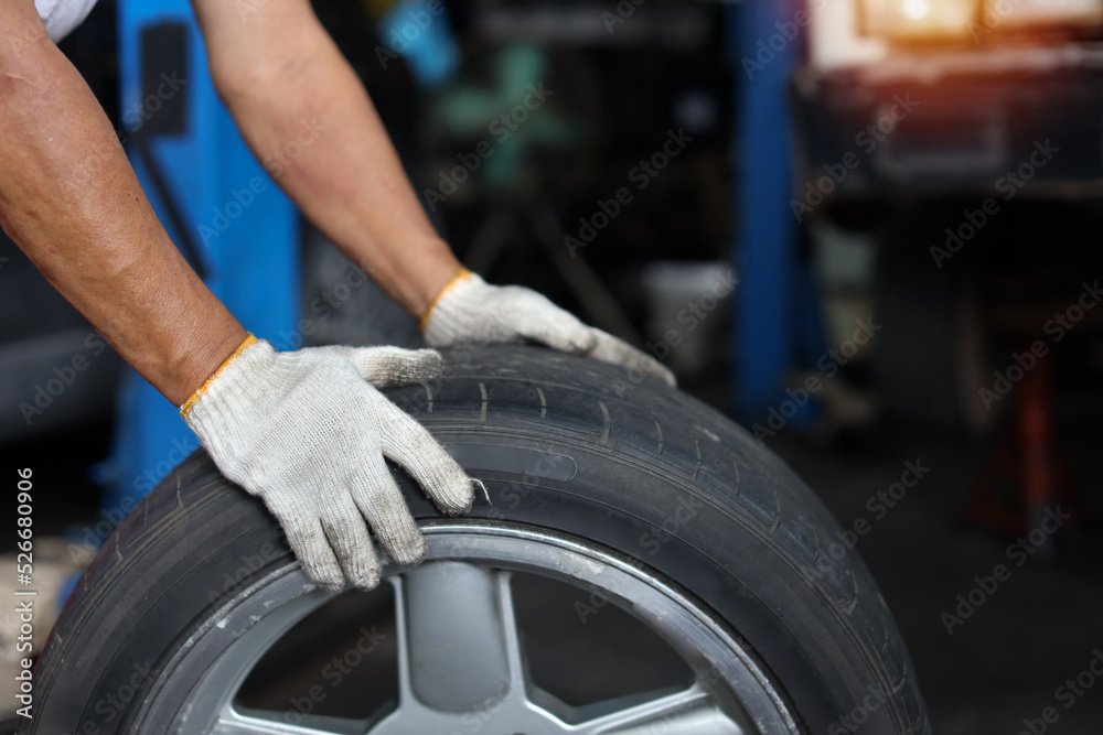 Man technician car mechanic hands in uniform holding tire for replacement or changeing at repair garage. Concept of car center repair service.