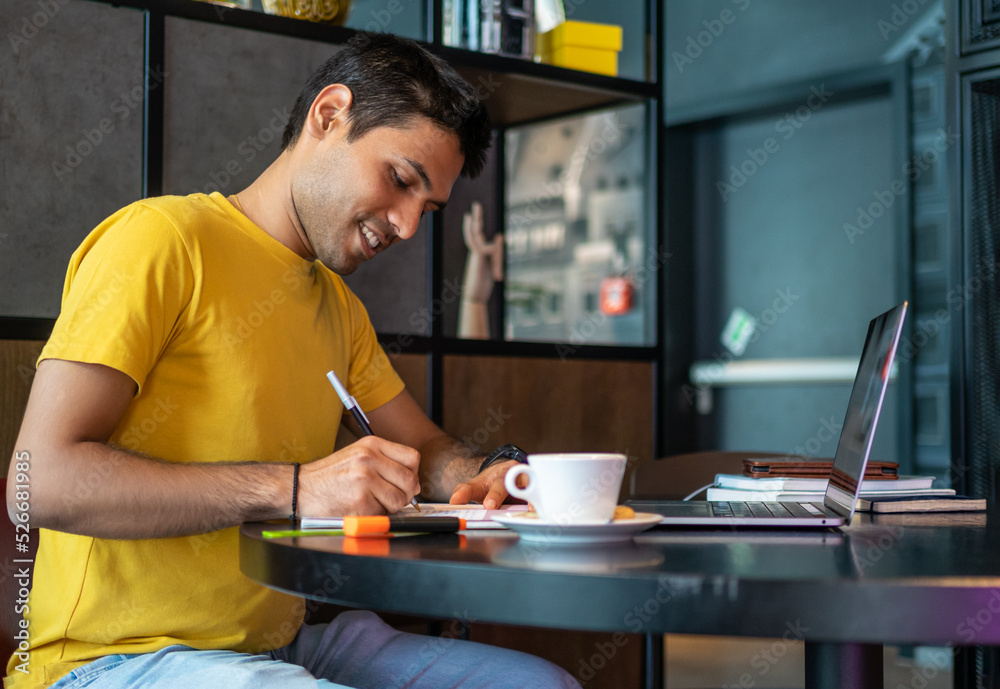 Fototapeta premium Cheerful Indian man smiling and making notes