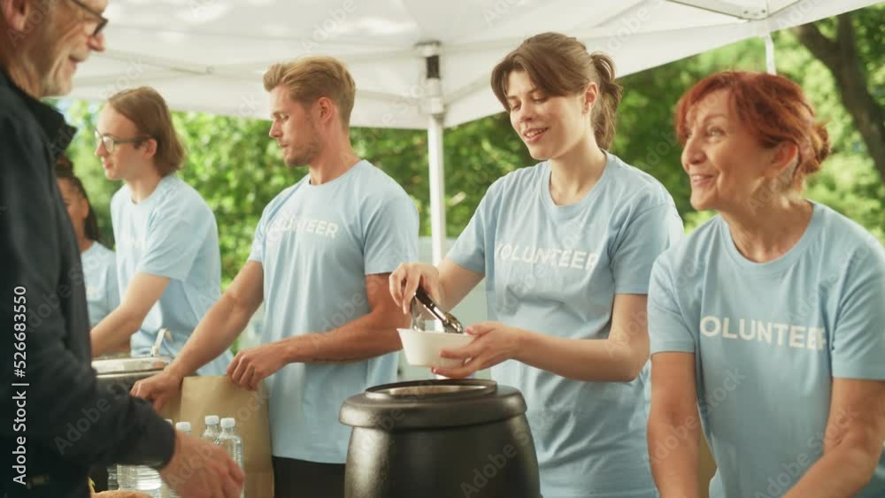 Happy Group of Young Adult Volunteers Serving Free Food for Poor People in Need. Charity Workers Help Members of the Community. Humanitarian Aid to Refugees and Immigrants. Slow Motion Footage.