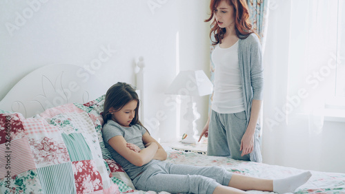 Foto Angry mother argue scolding her upset little daughter lying on bed in cozy brigh