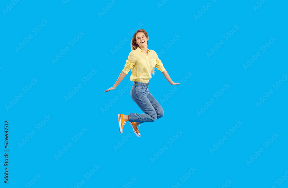 Fun and rejoice. Cheerful funny teen girl having fun bouncing isolated on light blue banner background. Woman in shirt, jeans and sneakers is in good mood and seems to be flying in air. Full length.