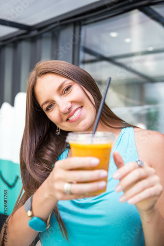 Authentic close up shot of happy young brunette long hair woman is drinking a fresh healthy dietetic biological natural orange juice from a transparent glass