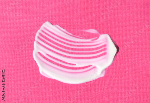 The texture of white cream on bright pink purple background. A smear of moisturizer closeup. Lotion swatch. Beauty, skin care product smear smudge drop. SPF sunscreen cream sample