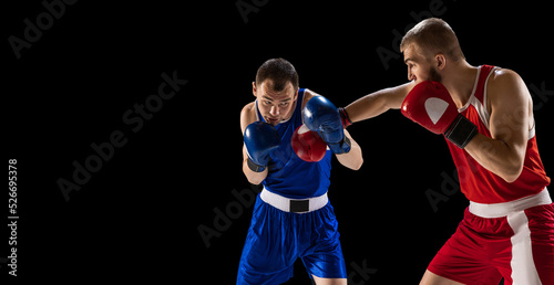 Fototapeta Naklejka Na Ścianę i Meble -  Young men, professional boxers in red and blue sports uniform boxing isolated on dark background. Concept of sport, skills, power, training, energy
