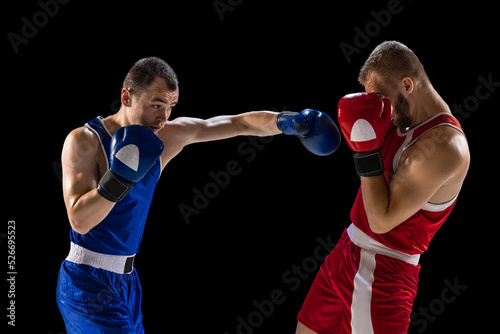 Young men, professional boxers in red and blue sports uniform boxing isolated on dark background. Concept of sport, skills, power, training, energy © master1305