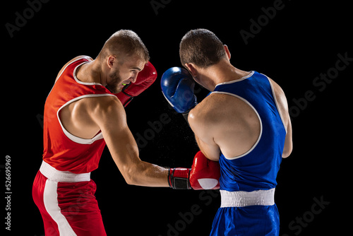 Training. Young professional boxers in red and blue sports uniform boxing isolated on dark background. Concept of sport, skills, power, training, energy © master1305