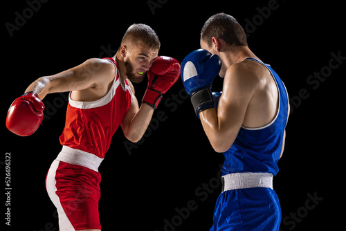Young men, professional boxers in red and blue sports uniform boxing isolated on dark background. Concept of sport, skills, power, training, energy