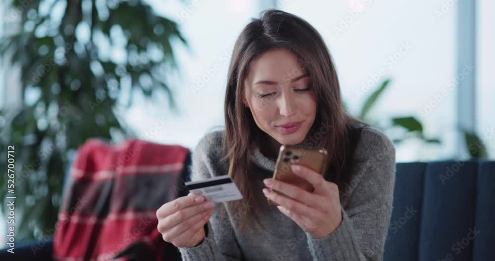 Young caucasian casual woman staying home in winter using smartphone paying for online food delivery service quickly and easily. Credit card payment. Young caucasian casual woman staying home in winter using smartphone paying for online food delivery service quickly and easily. Credit card payment.