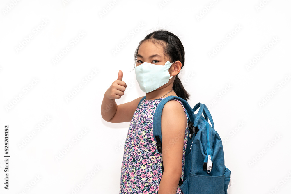 Portrait Asian child girl with facemask, carrying a blue backpack, show thumb up with confident, isolated portrait image on white background. The concept for back to school. Portrait Asian child girl with facemask, carrying a blue backpack, show thumb up with confident, isolated portrait image on white background. The concept for back to school.