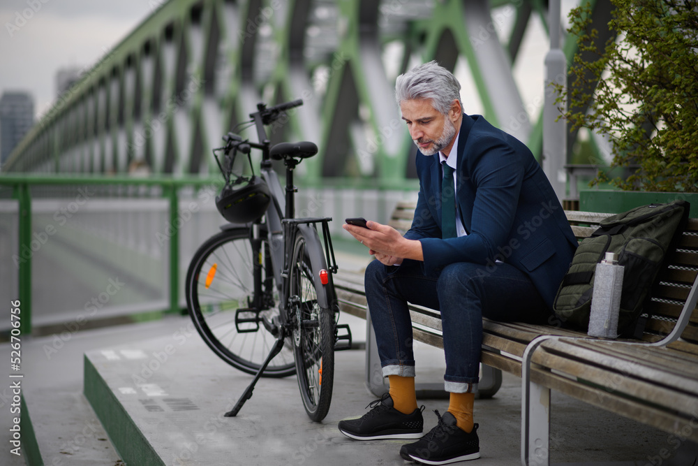 Businessman with bike sitting on bench, using smartphone. Commuting and alternative transport concept