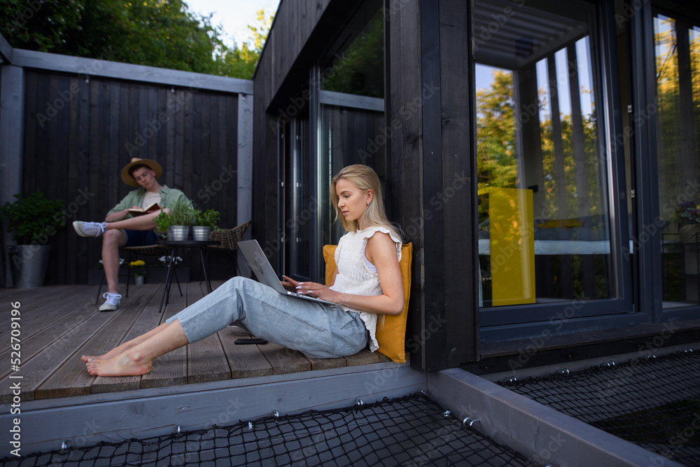 Happy young couple with laptop resting outdoors in a tiny house, weekend away and remote office concept.
