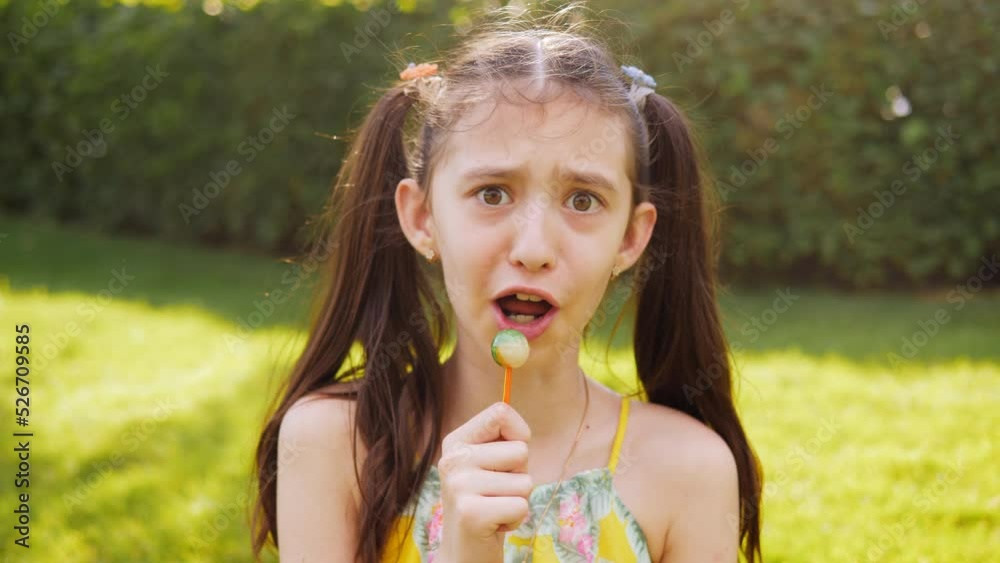 A preteen girl in the park licks a lollipop laughs and monkeys ...