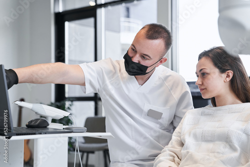 Calm woman looking at the laptop screen while doctor explaining to her steps of teeth whitening