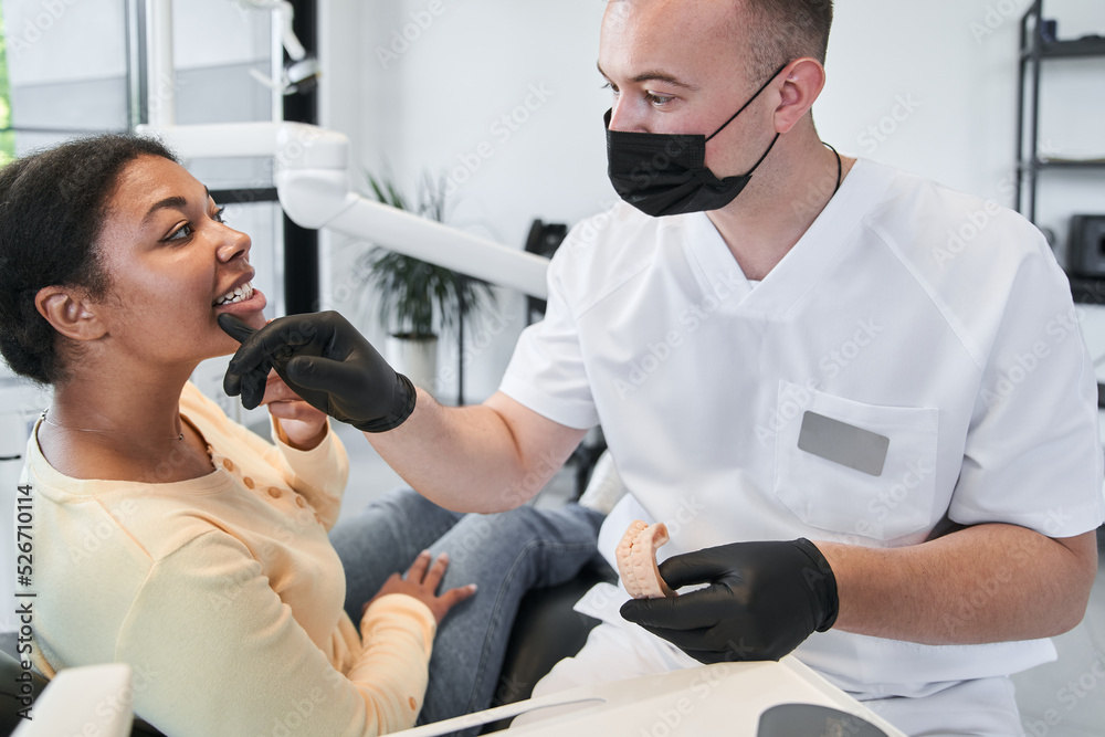 Doctor in protective equipment making check up of his female patient before whitening procedure Doctor in protective equipment making check up of his female patient before whitening procedure