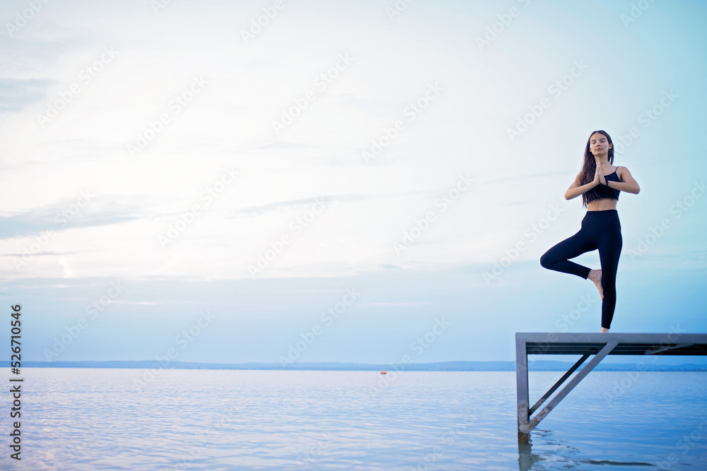 Young beautiful sportive girl meditating at early morning by the lake. Young beautiful sportive girl meditating at early morning by the lake.