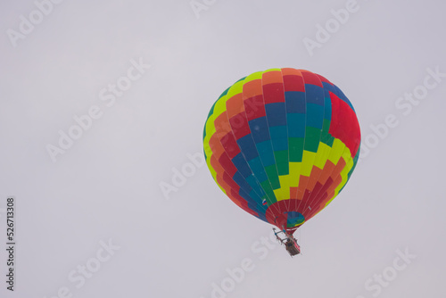Colorful rainbow hot air balloon flying against grey sky at Winter aerostat festival, snow falling. Freedom, sport, aircraft concept photo