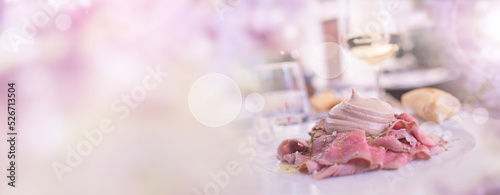 Vitello tonnato italien appetizer with restaurant view in a garden with bright bokeh. Horizontal tender pink background for a wedding catering.