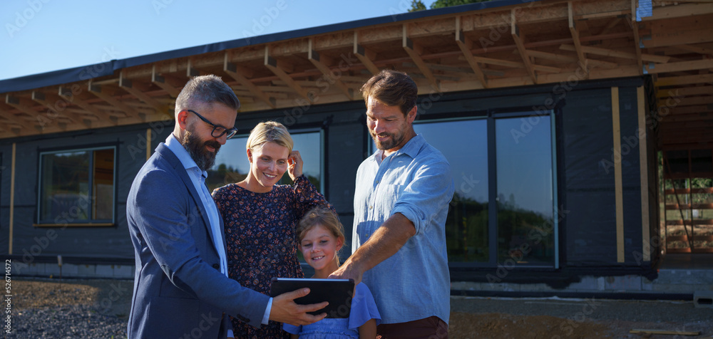 Sales Agent showing plans of new house to young family on construction site.