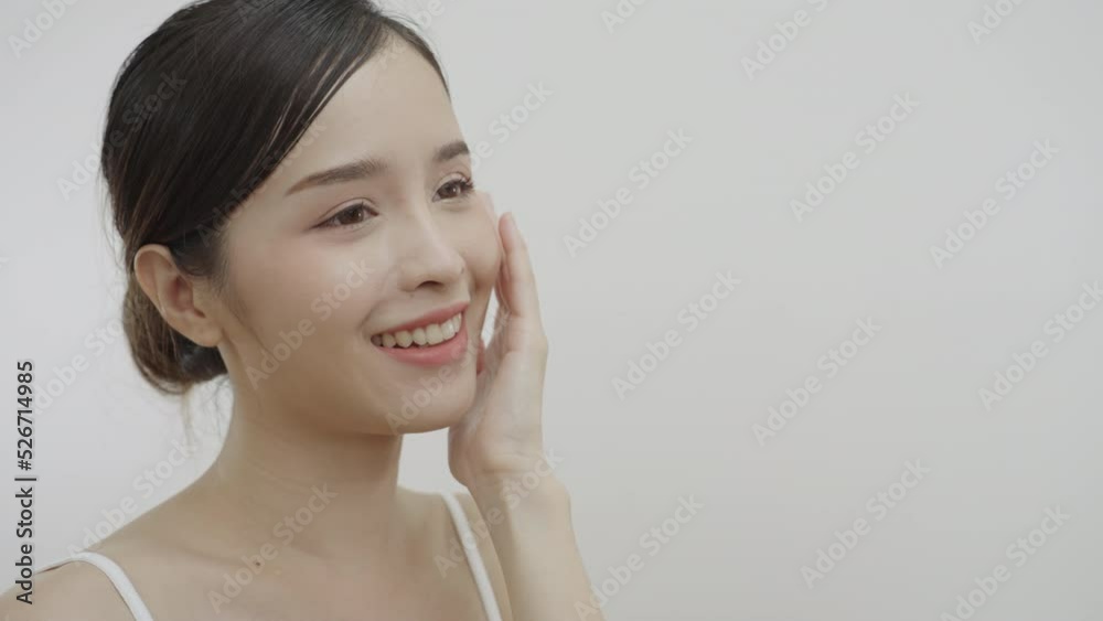 Close-up beauty portrait of beautiful Asian woman look at camera, smiling, touching face and healthy skin in slow motion, wellness, natural cosmetic skincare products. Close-up beauty portrait of beautiful Asian woman look at camera, smiling, touching face and healthy skin in slow motion, wellness, natural cosmetic skincare products.