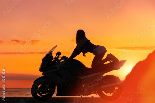 Silhouette of sexy young woman posing on the motorcycle. Golden sunset and motorbike on the background. Concept of World Motorcyclist Day and moto trips