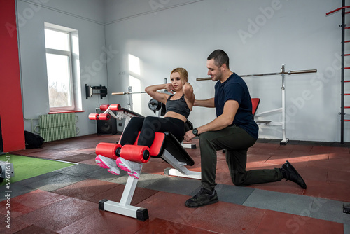 The trainer assists with female client doing workout in the gym