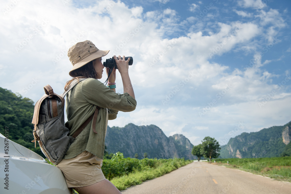 A young woman using black binoculars outside her car on the road of travel