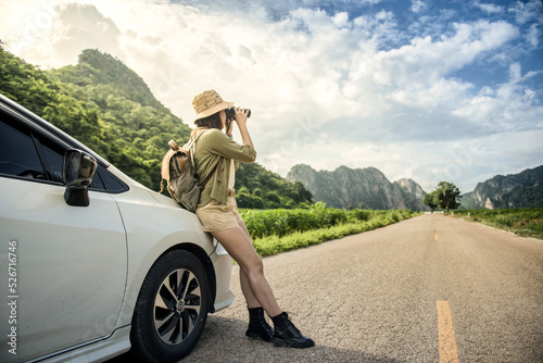 A young woman using black binoculars outside her car on the road of travel