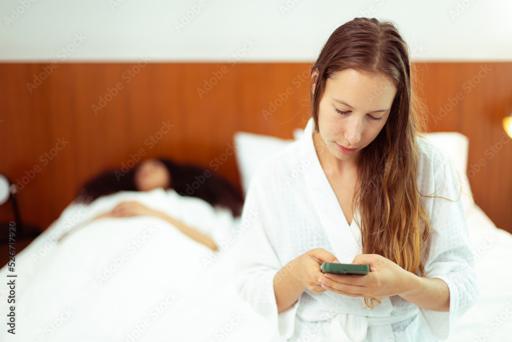 Caucasian and black women love together and lying on bed as diversity person. Young Adult Romantic couple check smart phone behind her back for secret chat text as jealous feeling, copy space Caucasian and black women love together and lying on bed as diversity person. Young Adult Romantic couple check smart phone behind her back for secret chat text as jealous feeling, copy space