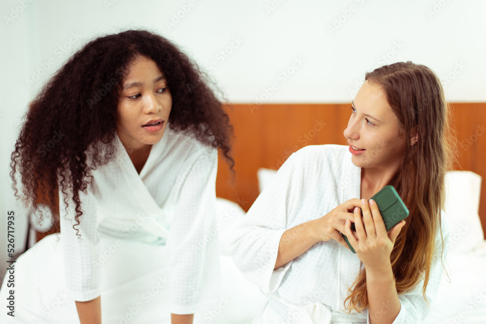 Caucasian and black women love together and lying on bed as diversity person. Young Adult Romantic couple check smart phone behind her back for secret chat text as jealous feeling, copy space Caucasian and black women love together and lying on bed as diversity person. Young Adult Romantic couple check smart phone behind her back for secret chat text as jealous feeling, copy space