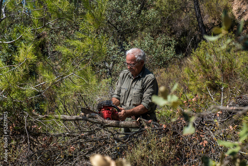 Hombre mayor cortando con la motosierra en el bosque, tercera edad activo