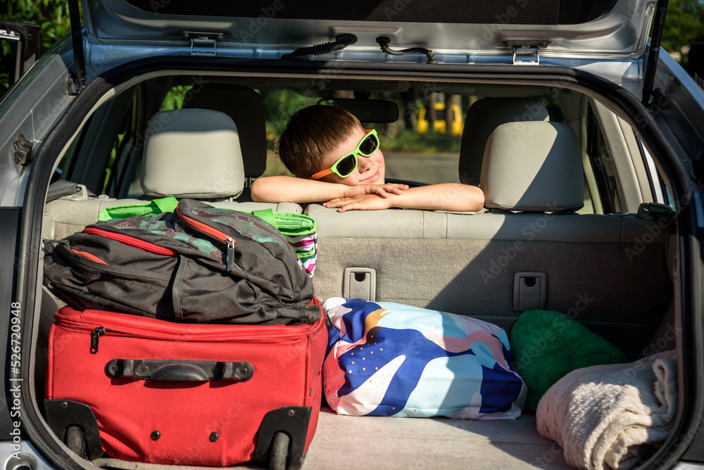 Adorable kid boy wearing sunglasses sitting in car trunk. Portrait of Happy child with open car boot while waiting for parent get ready for vocation. Family trip traveling by car concept Adorable kid boy wearing sunglasses sitting in car trunk. Portrait of Happy child with open car boot while waiting for parent get ready for vocation. Family trip traveling by car concept