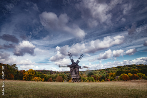 Rural summer autumn landscape with a windmill on a field with trees, sky and clouds. Old wooden windmill in an agricultural landscape. Old fashioned wooden windmill. Ukraine, Kyiv, Pirogovo
