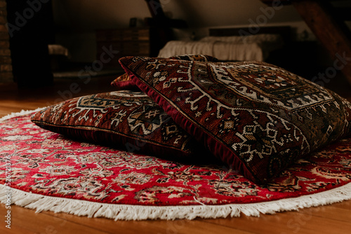 Two red persian bed pillows on a round hand knitted rug on the floor. Home decoration detail, copy space. Colorful carpet and textile. 