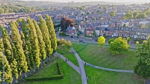 Cyclist on the gray bike path takes the exit into Hillsborough Park with a densely populated residential area in the background among the hilly landscape lit by the low sun. Drone lifting shot photo