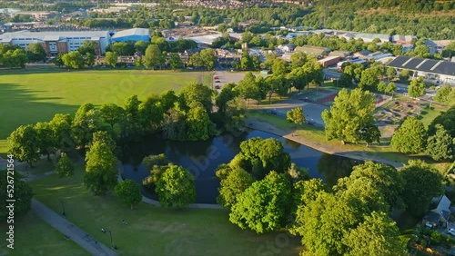 Large pond among the long shadows in a Hillsborough city park with the large Sheffield football stadium in the background among the hilly countryside in England. Drone lifting tilt shot photo